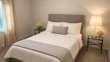 A neatly made bed with a grey headboard, two bedside tables with lamps and flower vases, and a window with curtains.