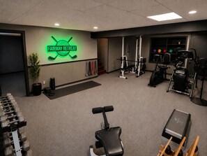 A gym with a neon sign, weight racks, exercise equipment, and a treadmill.