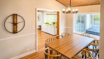 A dining area with a wooden table and chairs, a wooden ceiling, and a view of a kitchen and outdoor patio.