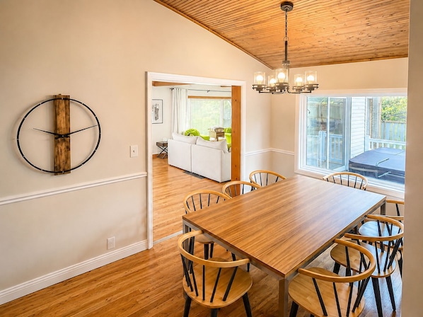 A dining area with a wooden table and chairs, a wooden ceiling, and a view of a kitchen and outdoor patio.