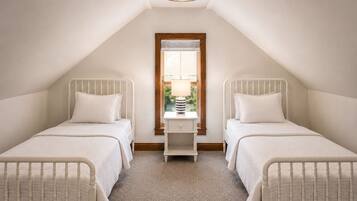A bedroom with two single beds, a window with blinds, a bedside table with a lamp, and a ceiling light fixture.