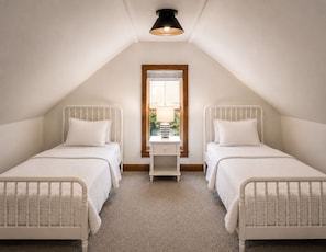 A bedroom with two single beds, a window with blinds, a bedside table with a lamp, and a ceiling light fixture.