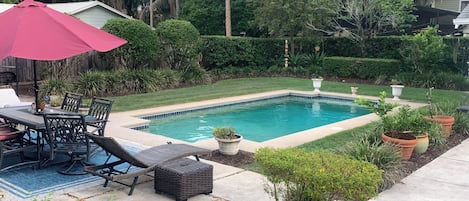 Un jardin avec une piscine, des meubles de patio et un parasol rouge.