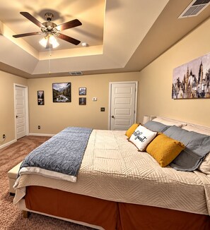 A bedroom with a bed, a ceiling fan, a door, and a wall with pictures.