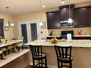 A kitchen with dark wood cabinets, a granite countertop, and a stainless steel stove. There is a dining area with a white table and chairs.