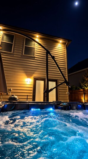 Un jacuzzi avec des lumières bleues, situé devant une maison dotée d’un toit en pente et d’un porche.