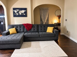 A living room with a sectional sofa, a small table with a vase, and a world map artwork on the wall.