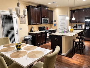 A modern kitchen with dark wood cabinets, a central island, and a dining area with a white table and chairs.