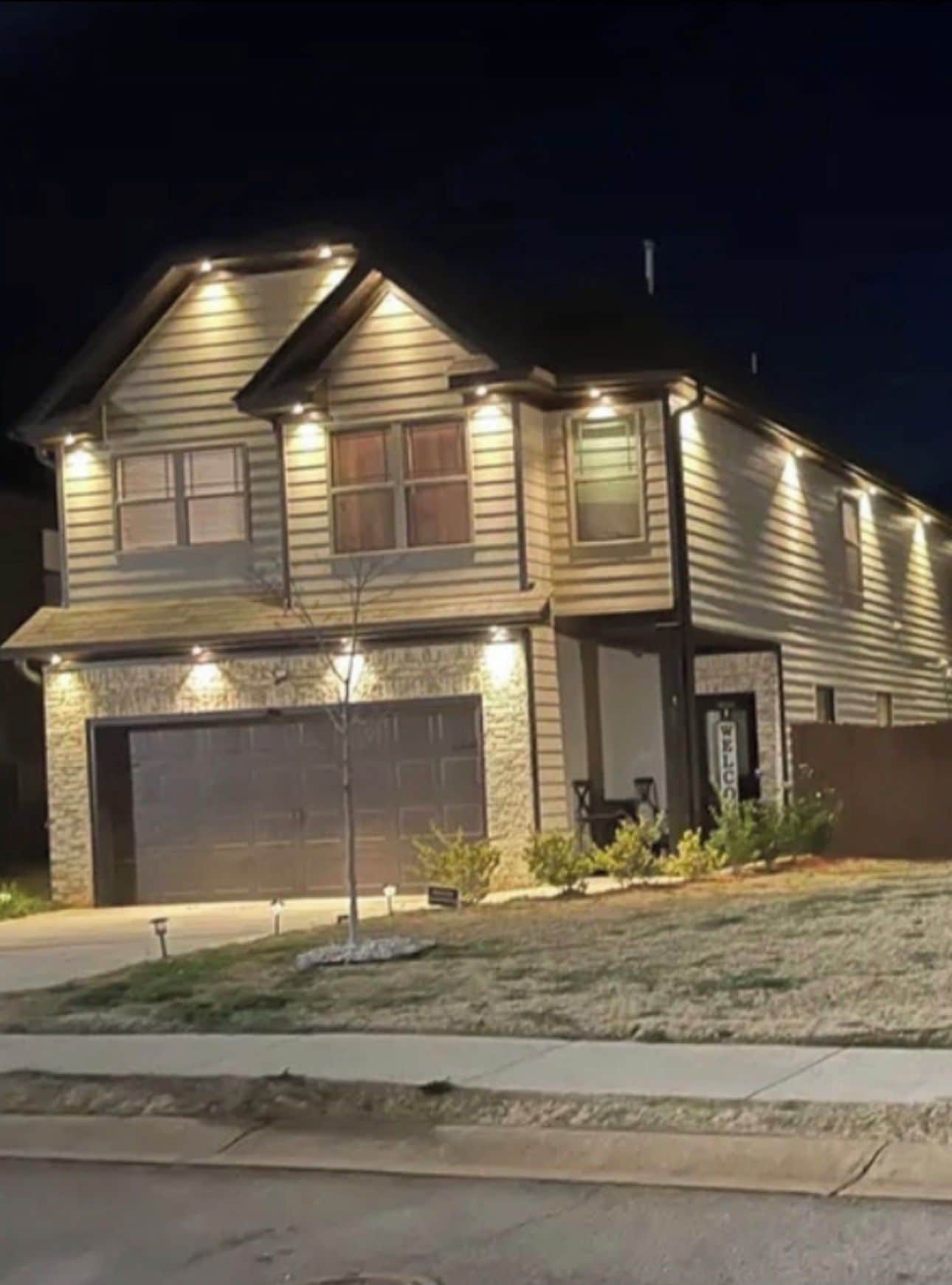 A two-story house with a garage, a stone foundation, and a well-lit front porch.