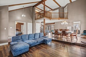 A spacious living area with a large sectional sofa, wooden flooring, and a high ceiling with exposed beams. - Big St. Charles Gateway-Deer/Forest View (Saint Charles)