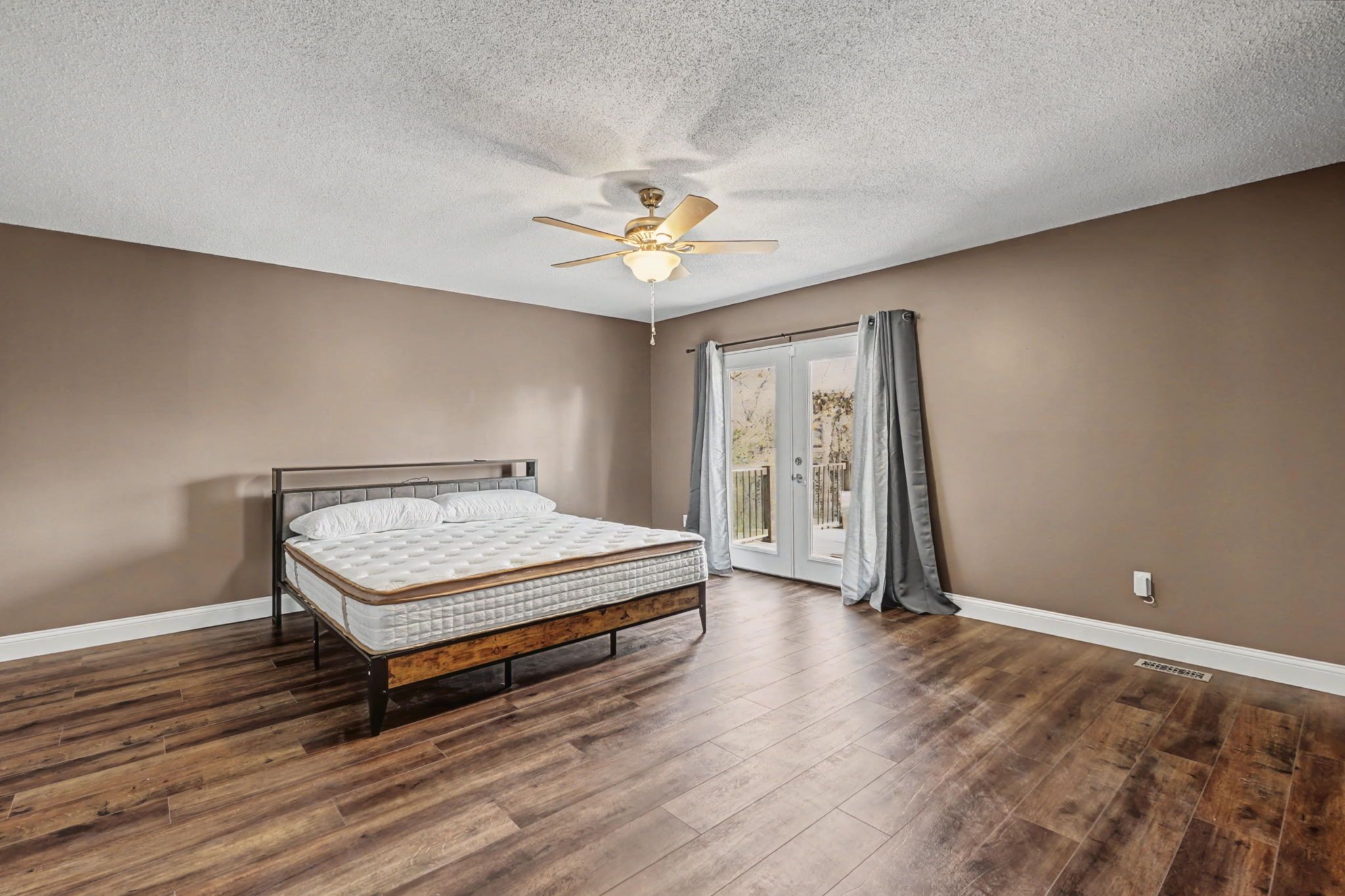 Un dormitorio con cama, piso de madera, ventilador de techo y puerta que da a un balcón.