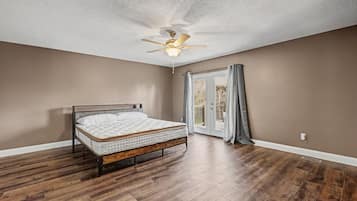 Un dormitorio con cama, piso de madera, ventilador de techo y puerta que da a un balcón.