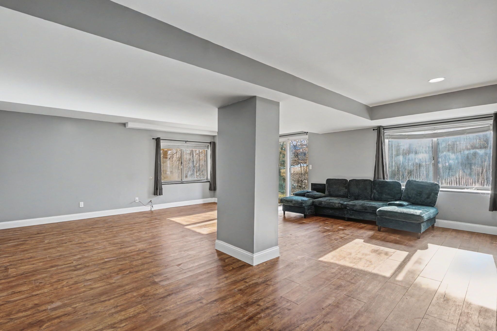 A spacious living area with hardwood flooring, a sectional sofa, and large windows.