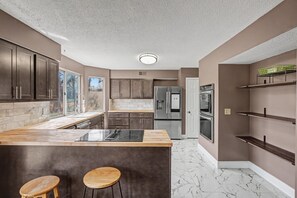 A modern kitchen with dark cabinets, a marble countertop, a built-in stove, and a refrigerator. - Big St. Charles Gateway-Deer/Forest View (Saint Charles)