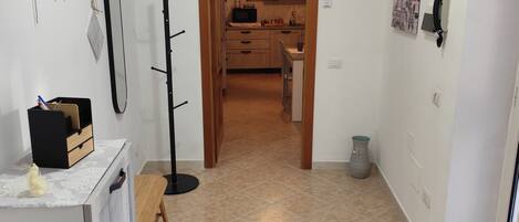 A hallway leading to a kitchen with a microwave, a small table, and a chair.