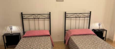 A double room with two beds, each with a patterned bedspread and a pink pillow. There are two bedside tables with lamps.