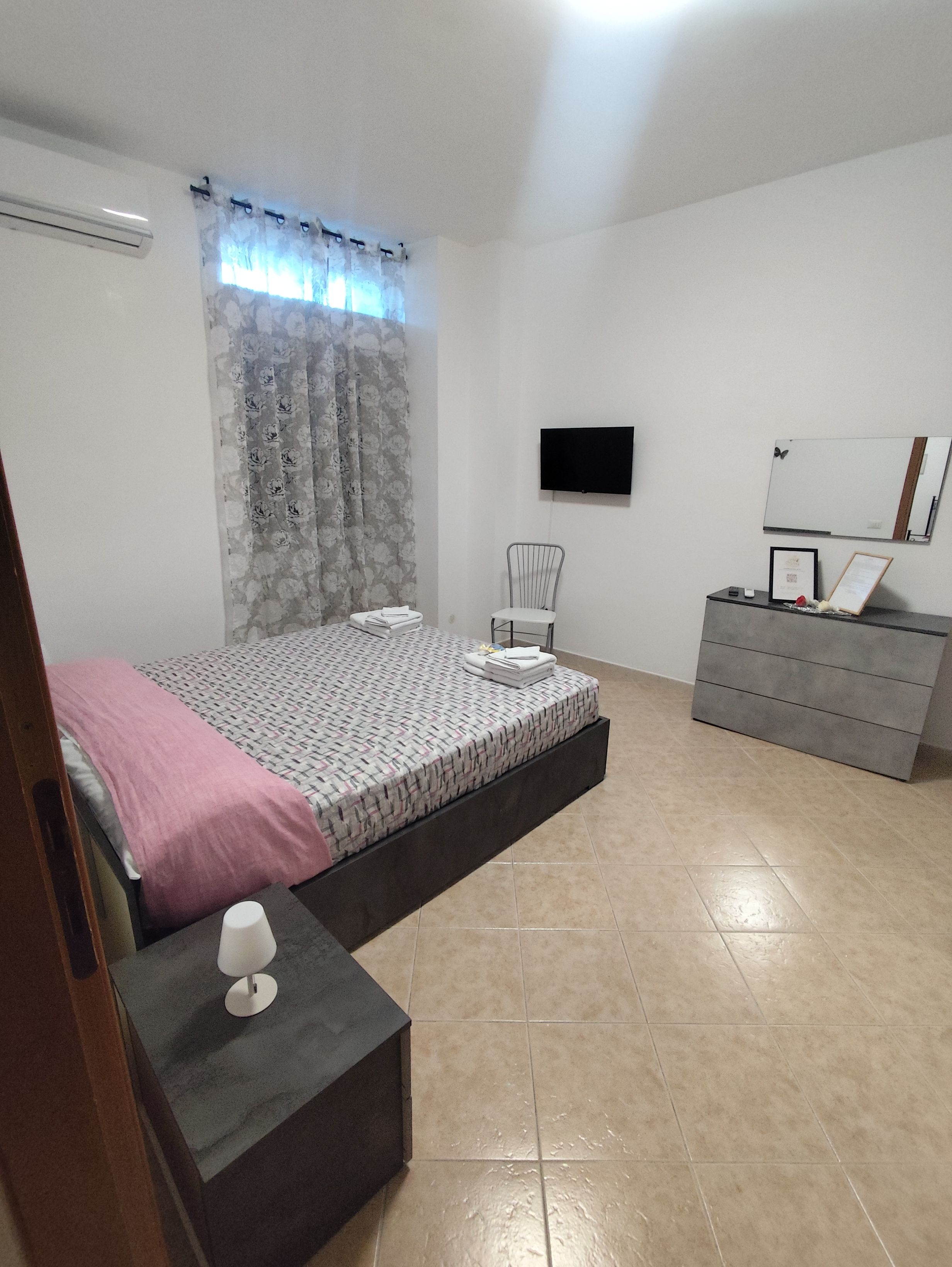 A bedroom with a bed, a bedside table, a dresser, a TV, and a mirror.