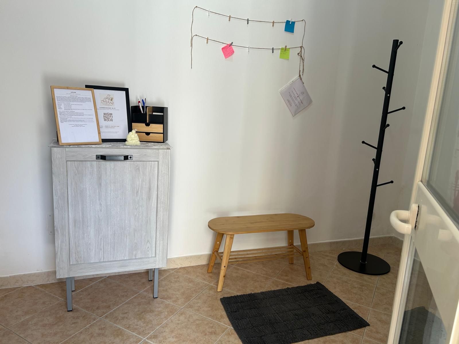 Une pièce avec un meuble en bois, un petit tabouret, un porte-manteau et un tapis noir.