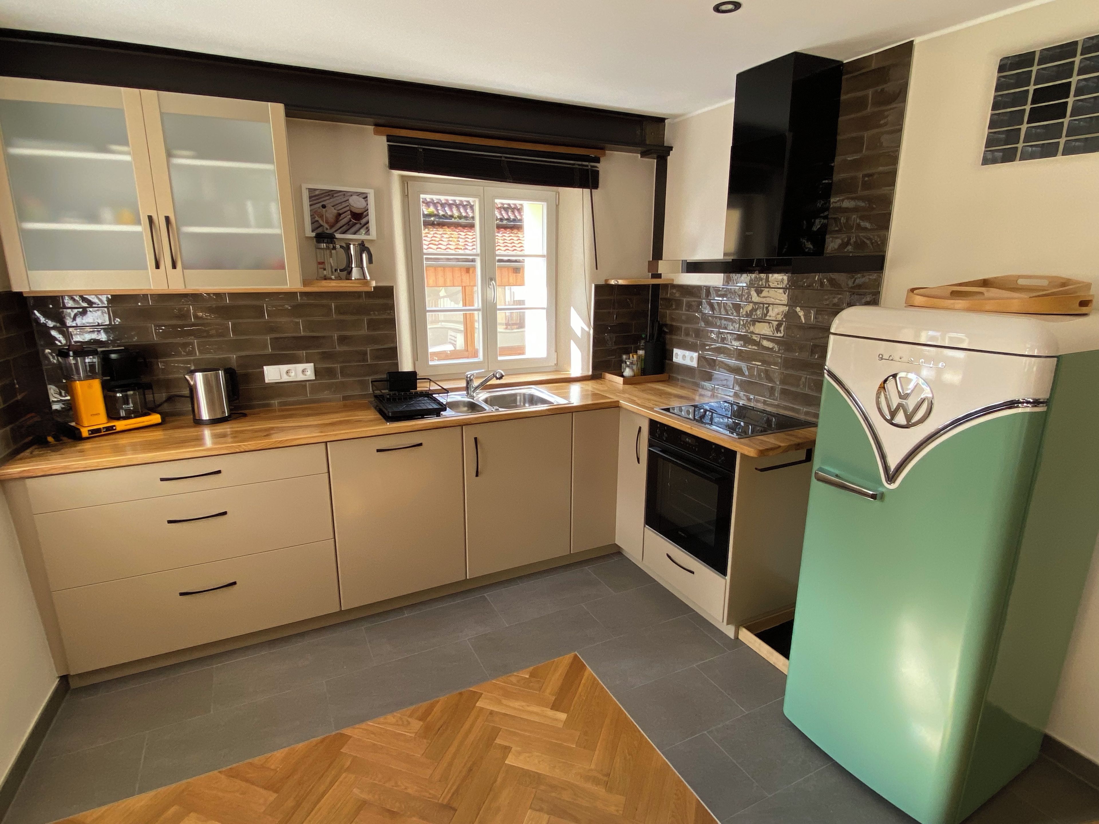 A kitchen with a vintage refrigerator, a coffee maker, and a window with a view of a house.