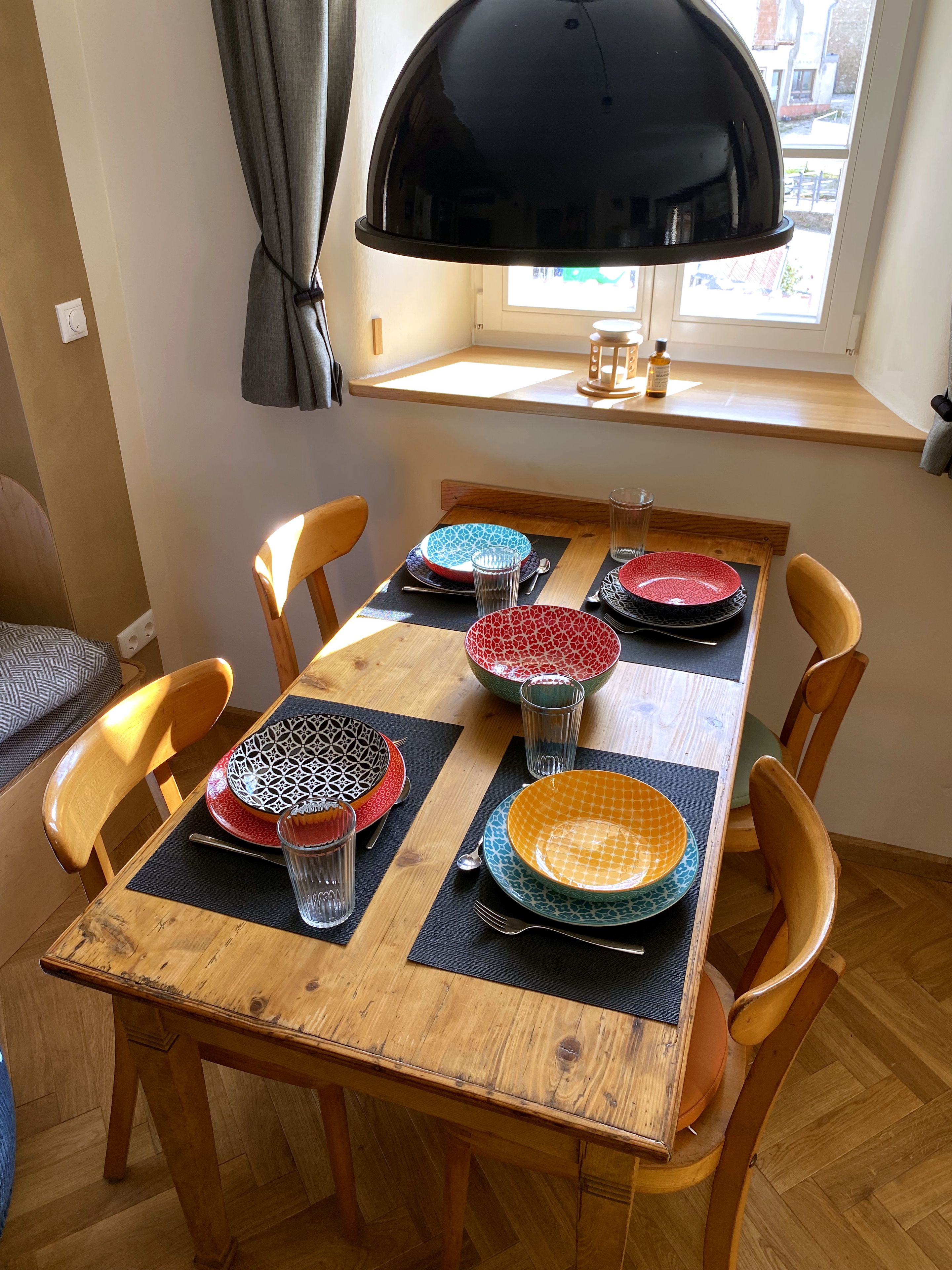 A dining table with six chairs, black placemats, and patterned plates.