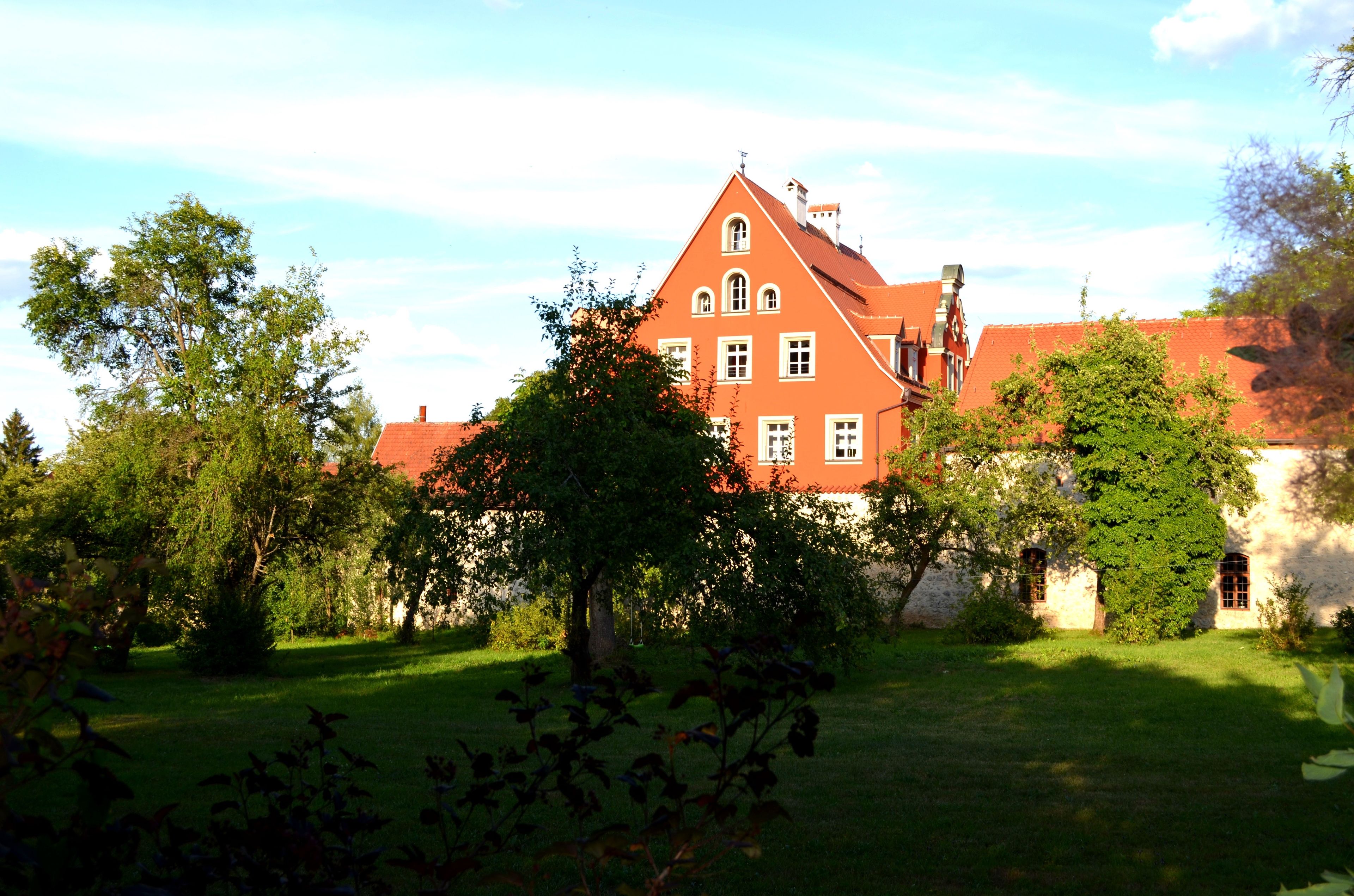 Un grand bâtiment à toit rouge, doté de nombreuses fenêtres, entouré d’une végétation luxuriante et d’arbres.