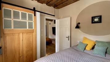 A bedroom with a wooden door, a bed with a quilted cover, and a wall-mounted lamp.