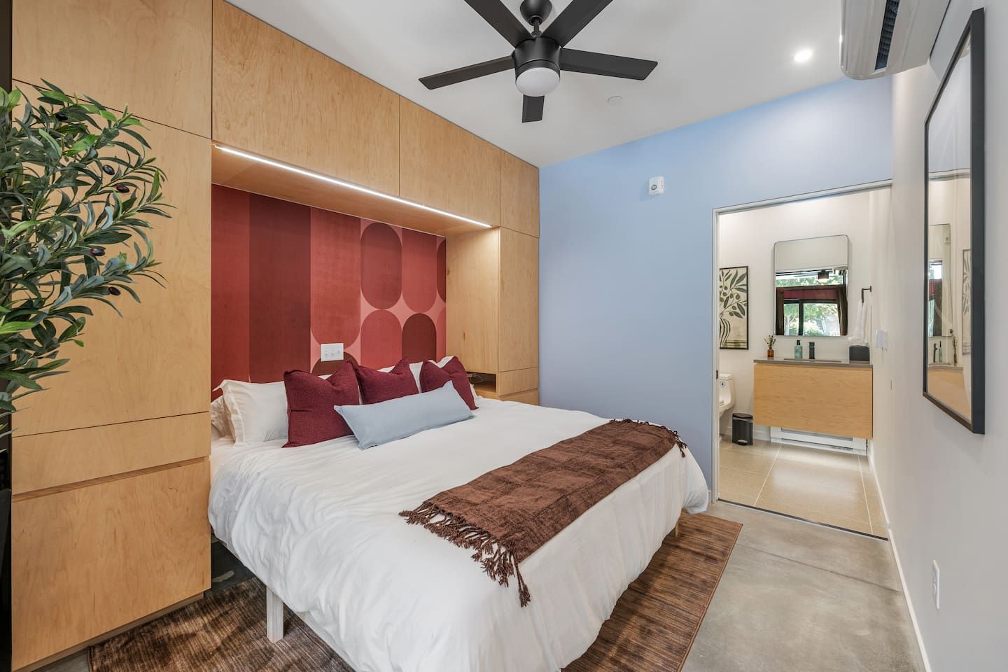 A modern bedroom with a bed, a ceiling fan, and a view into the bathroom.