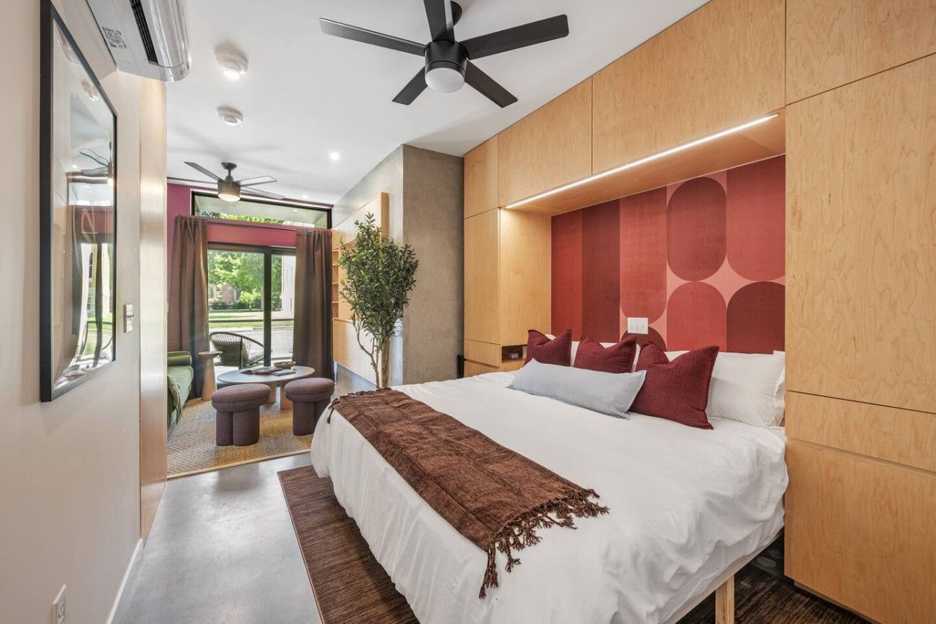 A modern bedroom with a large bed, a ceiling fan, and a view of the outdoors.