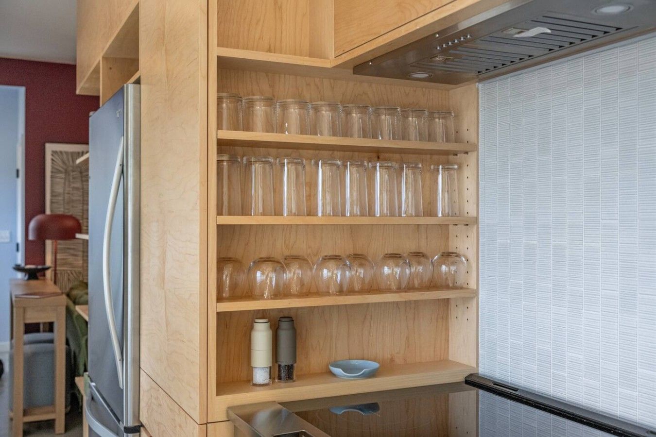 A kitchen with wooden shelves holding glass jars, a kettle, and a bowl.