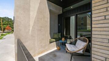 A modern outdoor seating area with a wicker chair and a small round table, a cushioned bench, and a potted plant.