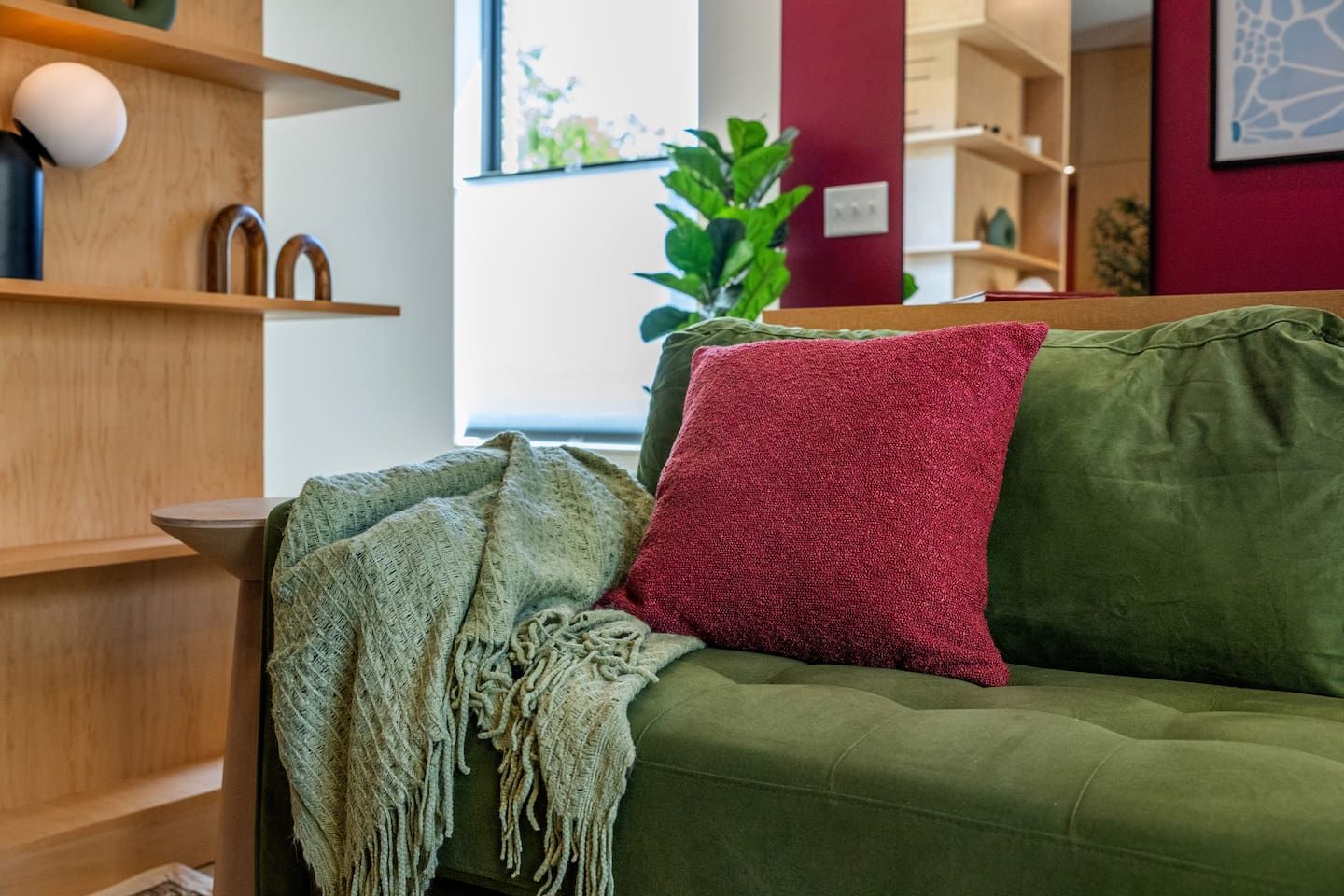 A green sofa with a red pillow and a fringed throw blanket.