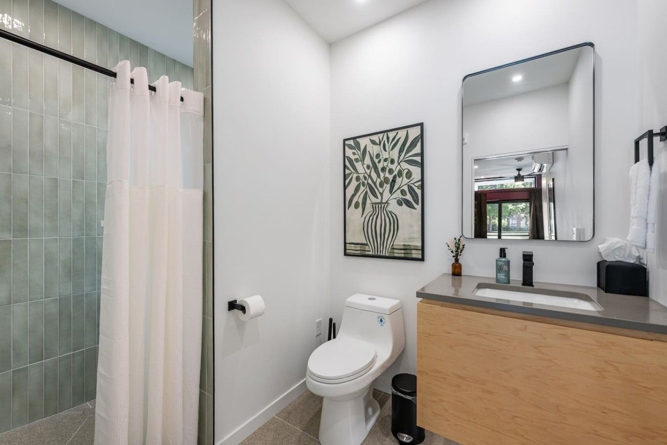 A modern bathroom with a glass shower enclosure, a toilet, a sink with a mirror, and a framed artwork on the wall.