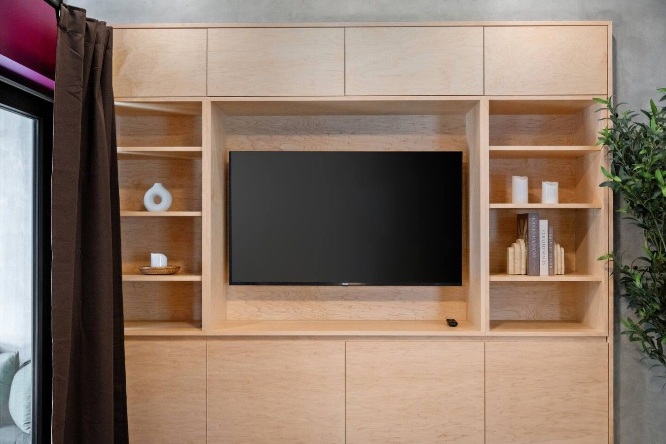A modern entertainment unit with a flat-screen TV, wooden shelves, and a small plant.