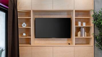 A modern entertainment unit with a flat-screen TV, wooden shelves, and a small plant.