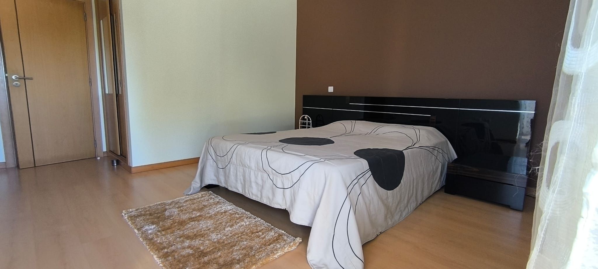 A bedroom with a bed, a TV, and a wooden floor.