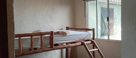 A bunk bed with a wooden ladder, a ceiling fan, and a window with a metal gate.