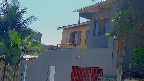 A two-story building with a grey facade, a red gate, and a balcony. - CASA CHARMOSA (Arraial d'Ajuda)