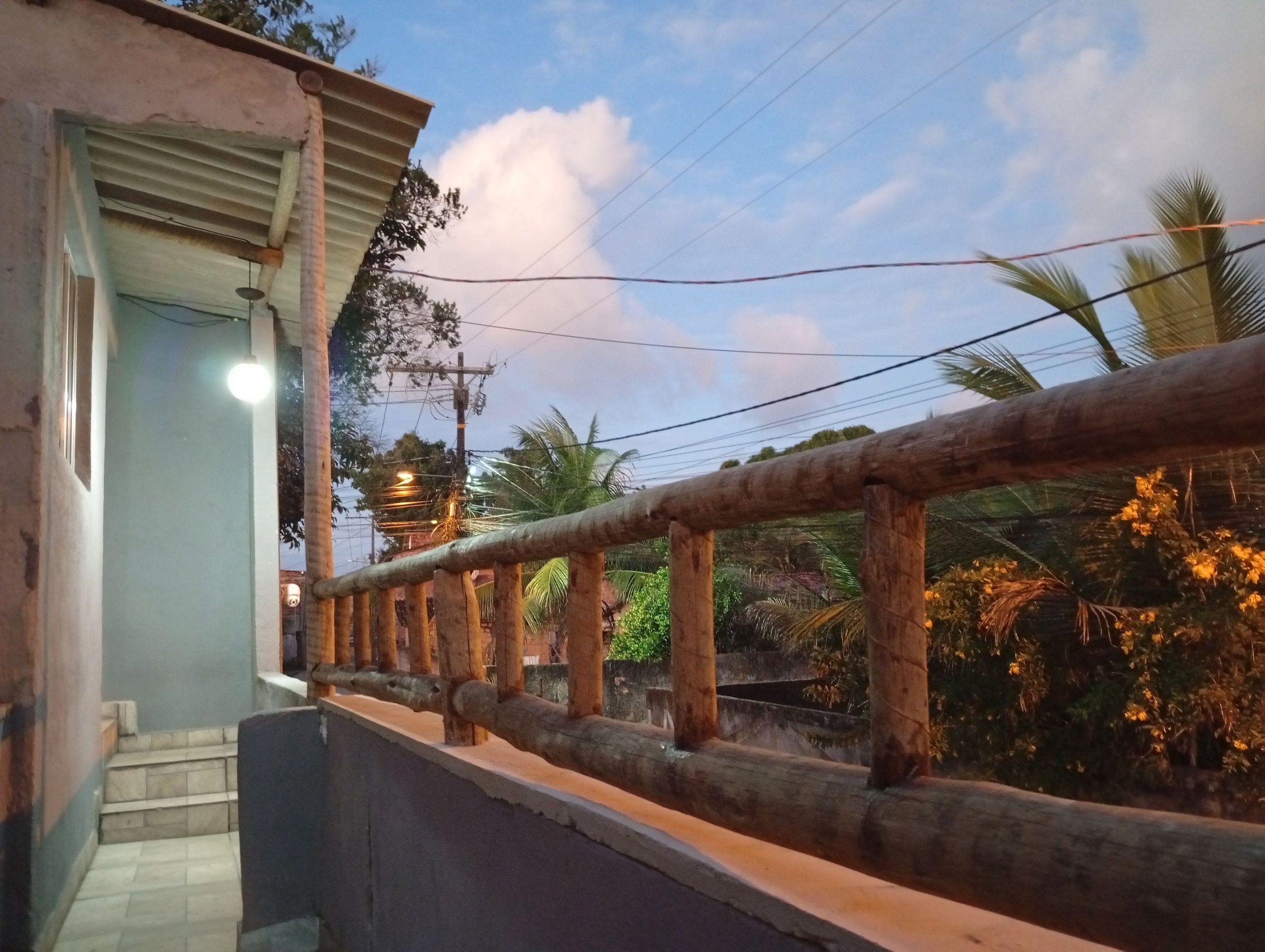 Un balcón con baranda de madera que da a un jardín con palmeras y cielo despejado.