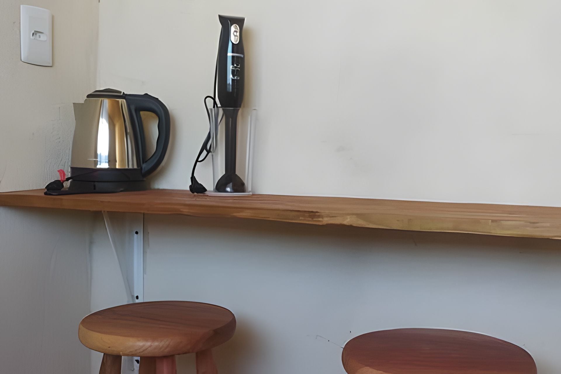 Una encimera de cocina con una tetera, una licuadora y dos taburetes de madera.