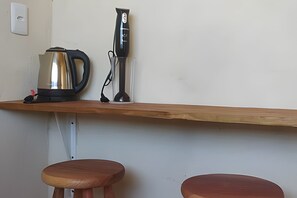 A kitchen counter with a kettle, a blender, and two wooden stools. - CASA CHARMOSA (Arraial d'Ajuda)