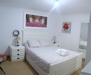 Ein Schlafzimmer mit einem Bett, zwei Nachttischen, einem Spiegel und zwei an der Wand hängenden Bildern.
