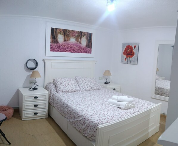 A bedroom with a bed, two bedside tables, a mirror, and two wall-mounted paintings.