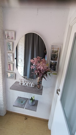 A room with a circular mirror, a 'Home' sign, and a small plant on a shelf.