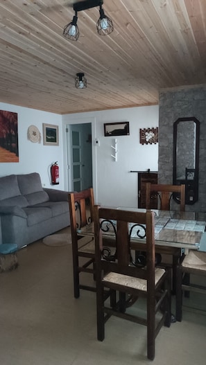 A dining area with a wooden table and chairs, a sofa, and a stone wall.