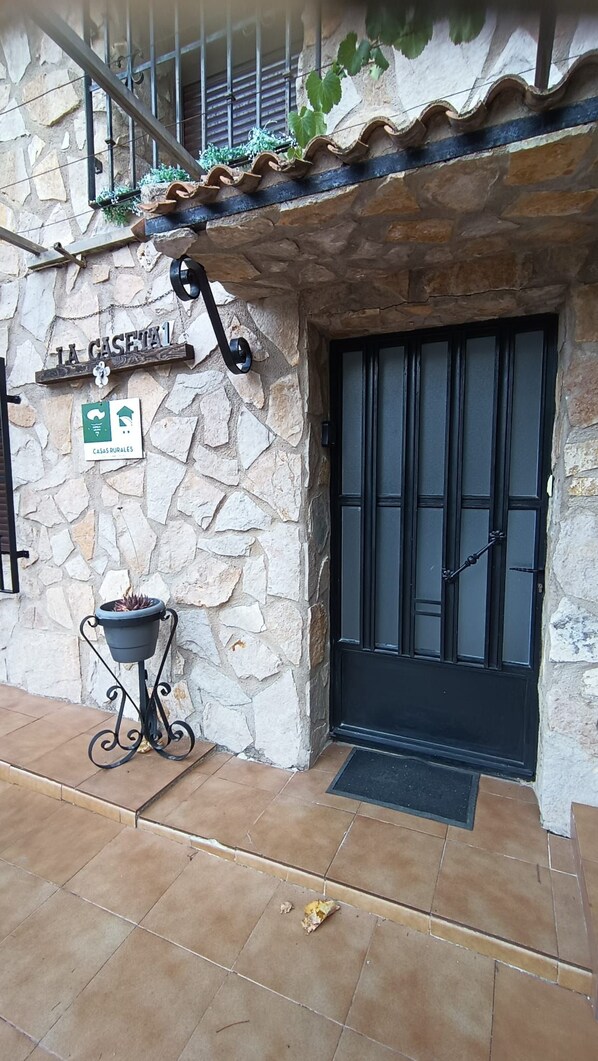 A rustic stone building with a black door, a sign indicating 'CASAS RURALES', and a potted plant on the ground.