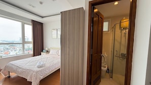 A hotel room with a bed, a window with curtains, a wooden door leading to a bathroom with a shower, and a city view. - 2 bedrooms AirPort view apartment  (Tan Son Hoa)