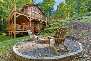 A cabin with a deck, a fire pit, and two Adirondack chairs.
