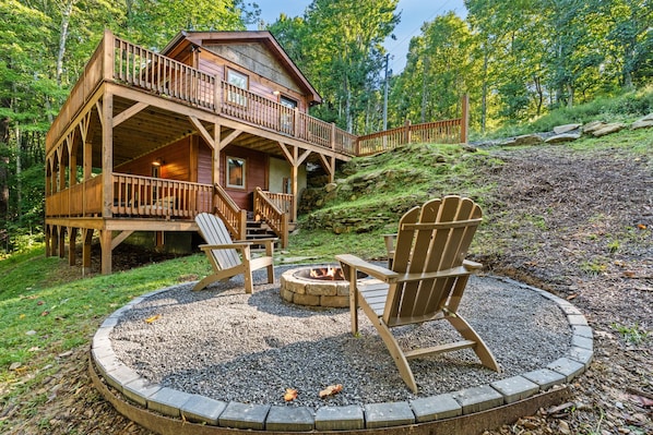 Una cabaña con terraza, un brasero y dos sillas Adirondack.