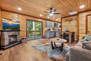 A cozy cabin interior with a fireplace, a dining area, a kitchen, and a large sliding glass door leading to a deck.