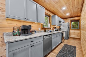 A modern kitchen with grey cabinets, a coffee machine, and a stainless steel refrigerator.